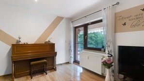 Huoneessa on piano, televisio, patteri ja ikkuna, jossa on verhot.