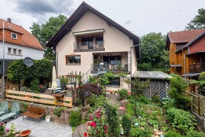Ein zweistöckiges Haus mit Balkon, Garten mit verschiedenen Pflanzen und Blumen sowie Holzzaun.