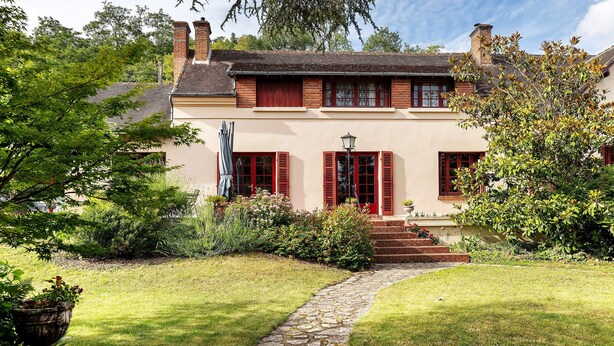 Een huis met een stenen pad dat naar een rode deur leidt, omringd door weelderig groen en een verzorgd gazon.