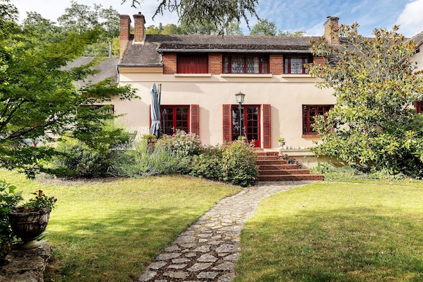 A house with a stone pathway leading to a red door, surrounded by lush greenery and a well-maintained lawn.