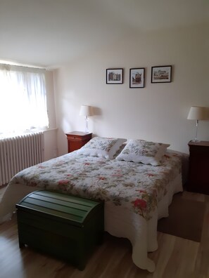 A bedroom with a bed, two bedside tables, a radiator, and a window with curtains.