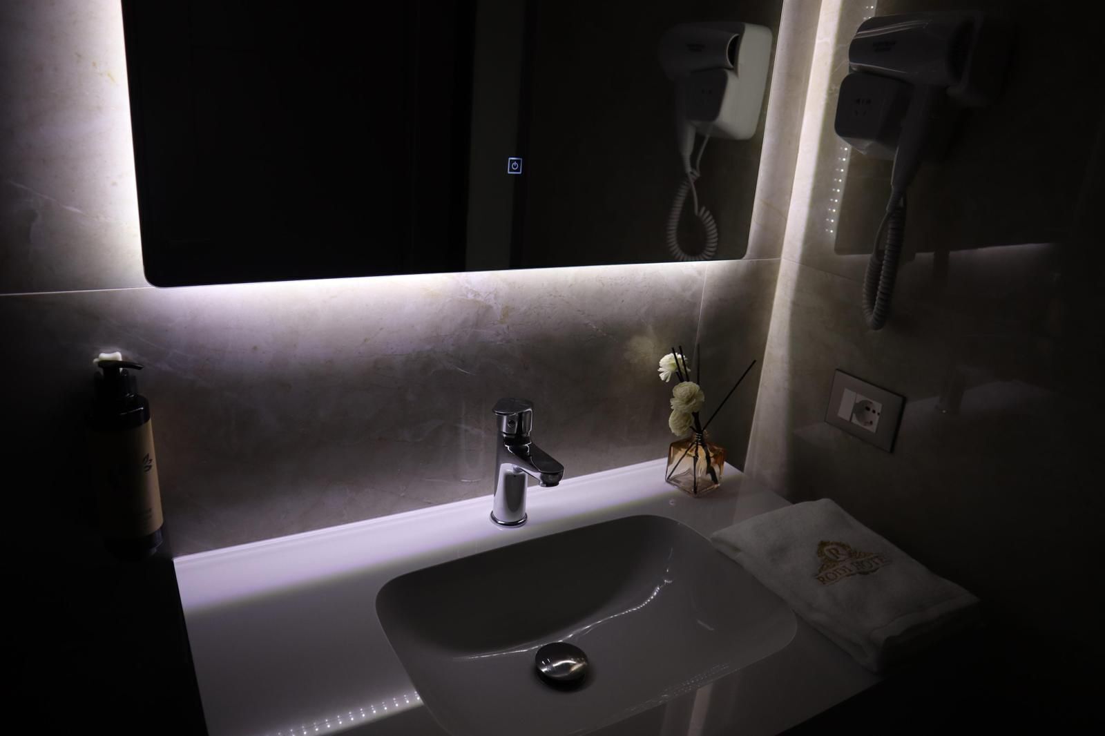 Baño con lavamanos, espejo y secador de pelo en la pared.