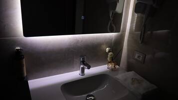 Baño con lavamanos, espejo y secador de pelo en la pared.