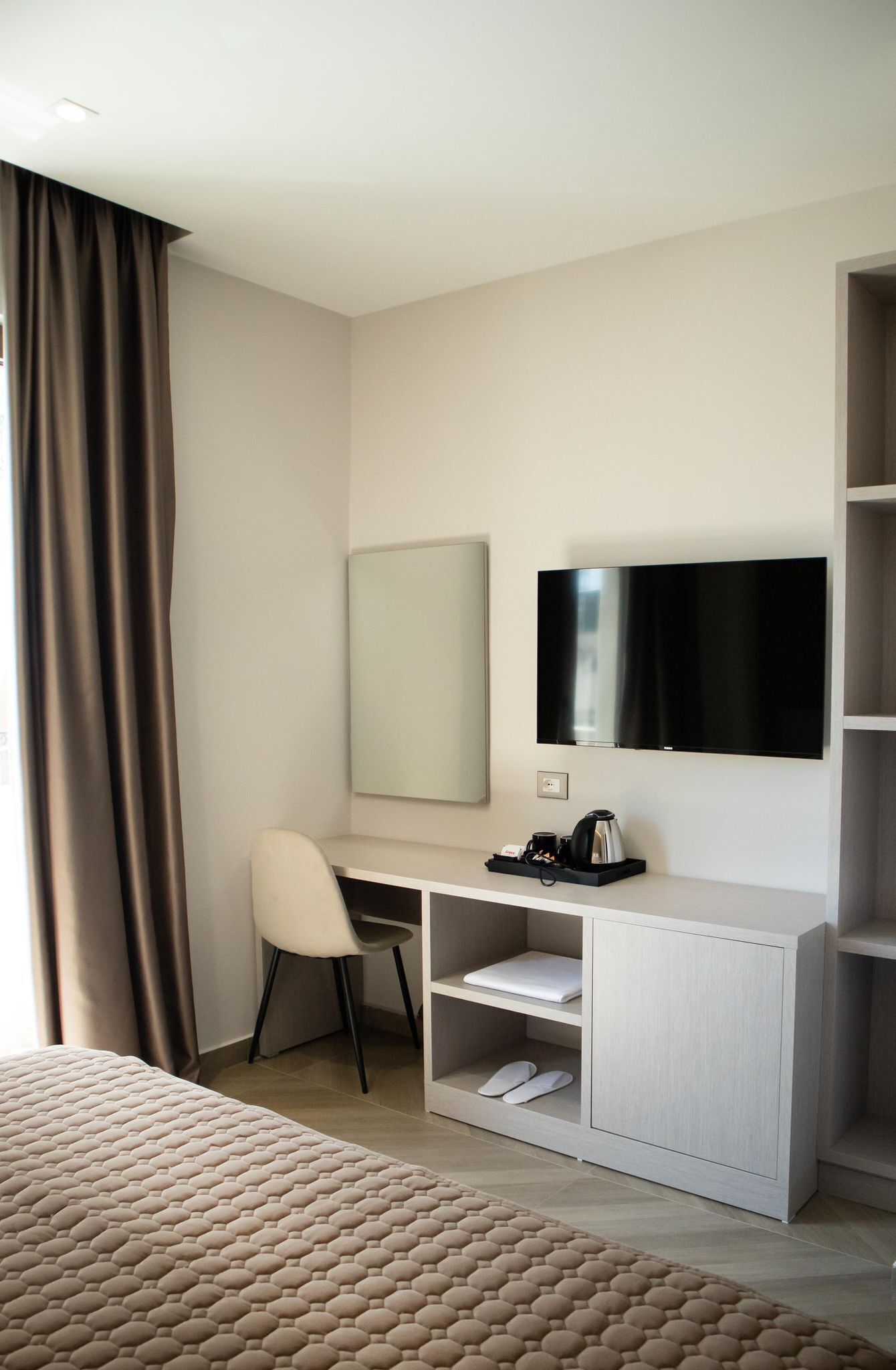 A hotel room with a bed, a desk with a chair, a television, and a shelf with a coffee maker.