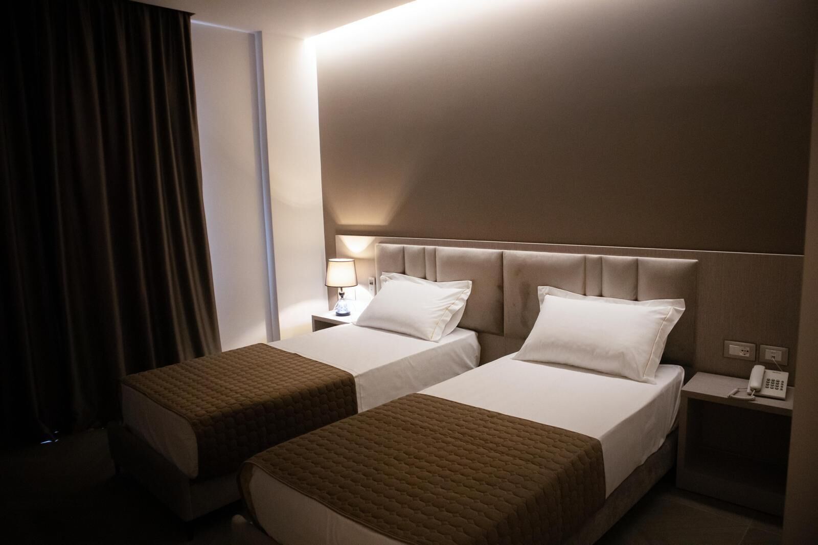 A hotel room with two beds, a nightstand with a lamp, and a phone.
