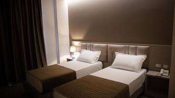 Una habitación de hotel con dos camas, una mesita de noche con lámpara y un teléfono.