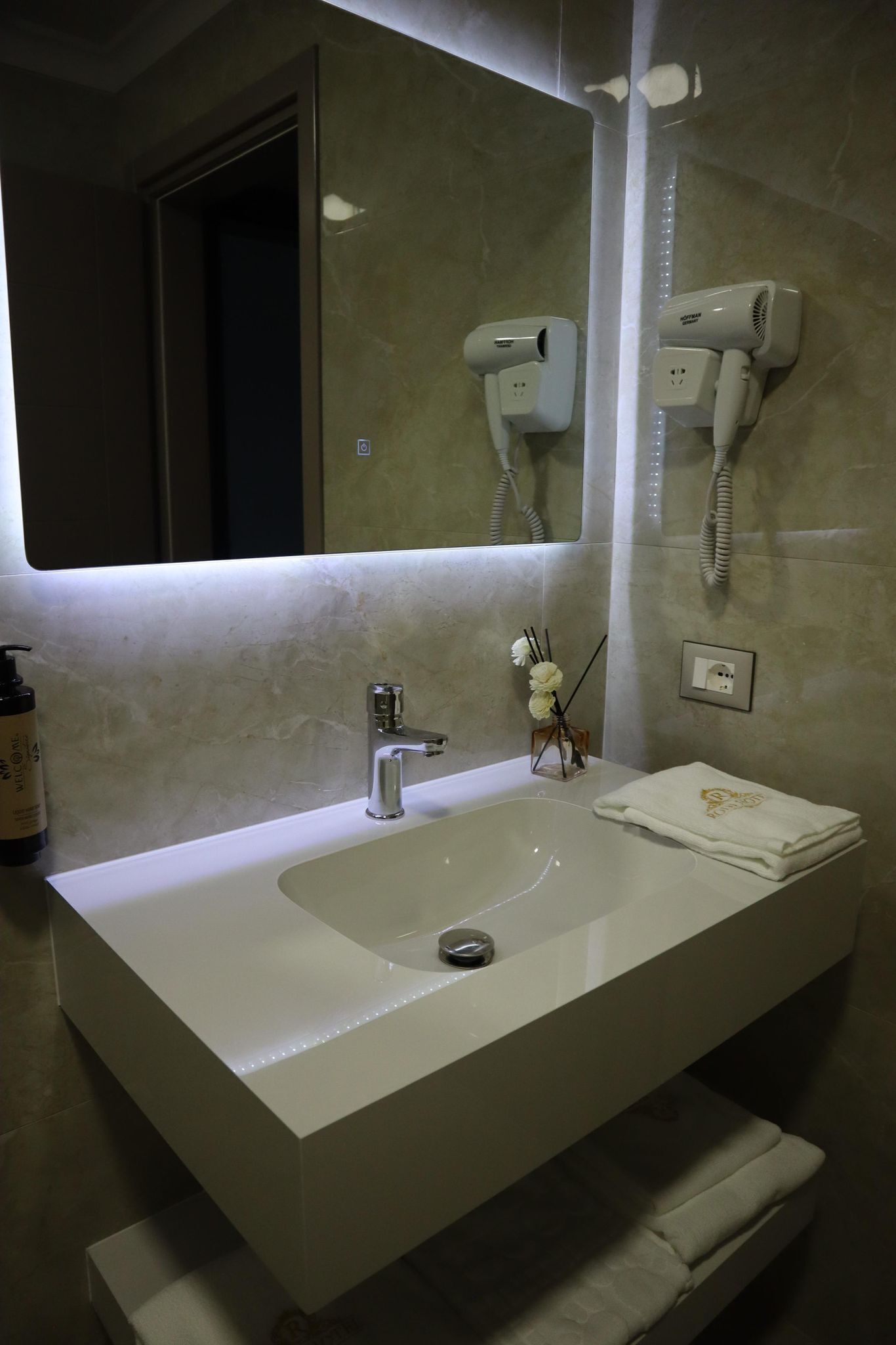 Un baño con un lavamanos blanco, un espejo, un secador de pelo y un perchero para toallas.