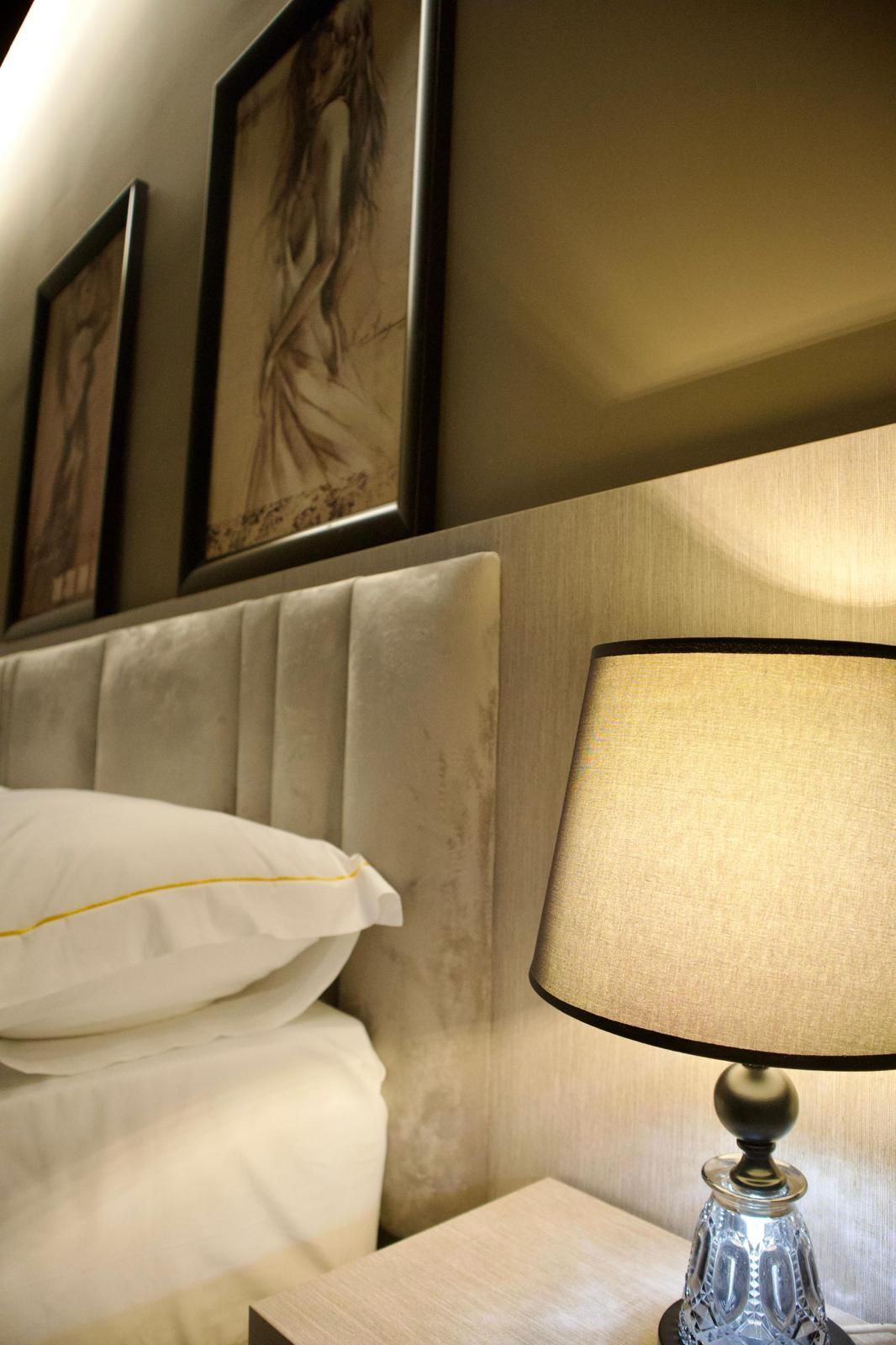 A hotel room with a bed, a nightstand, a lamp, and framed artwork on the wall.