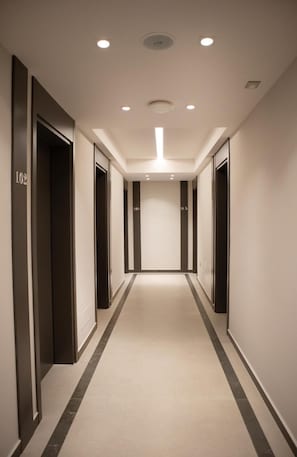 A modern hotel corridor with a central light fixture, dark doorways, and a carpeted floor. - Rodi Hotel Elbasan (Elbasan)