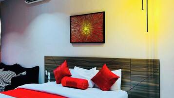 A modern hotel room with a large bed, a bedside table, a wall-mounted air conditioner, and a painting.