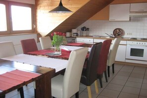 Ein Essbereich mit Tisch für vier Personen, Stühlen, Blumenvase und einer Küche im Hintergrund.