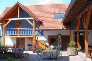 Ein zweistöckiges Gebäude mit rotem Ziegeldach, hölzernen Balkonen und einer Terrasse mit Gartenmöbeln.