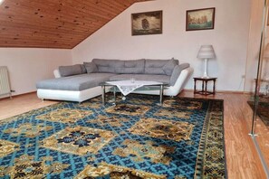 Ein Zimmer mit einer Eckcouch, einem Glastisch, einem gemusterten Teppich und zwei gerahmten Bildern an der Wand.