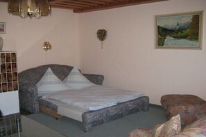 Ein Schlafzimmer mit einem Bett, einem Sessel, einem kleinen Tisch, einem Gemälde und einer Chandelier.