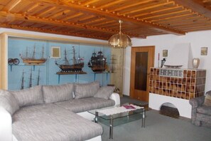 Ein Wohnzimmer mit Holzbalkendecke, einem grauen Sofa, einem Glastisch und einer Wand mit Schiffmodellen.
