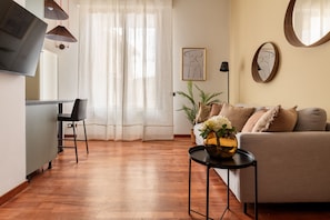 Ein modernes Wohnzimmer mit einer Couch, einem Couchtisch mit einer Vase, einem an der Wand montierten Fernseher und einem Essbereich mit Stuhl und Tisch.