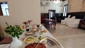A dining area with a table set for a meal, a sofa, and a television in the background. - Corte Mantovanella (Porto Mantovano)