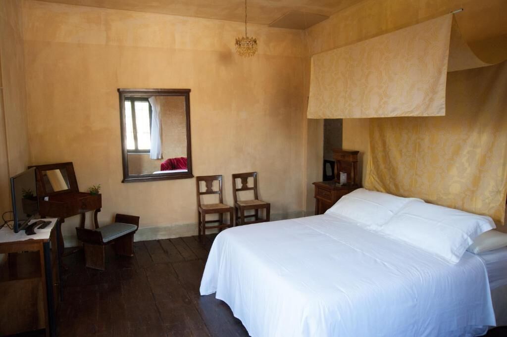 Ein Zimmer mit einem Bett, einem Schreibtisch mit Stuhl, einem Spiegel und einer Pendelleuchte.