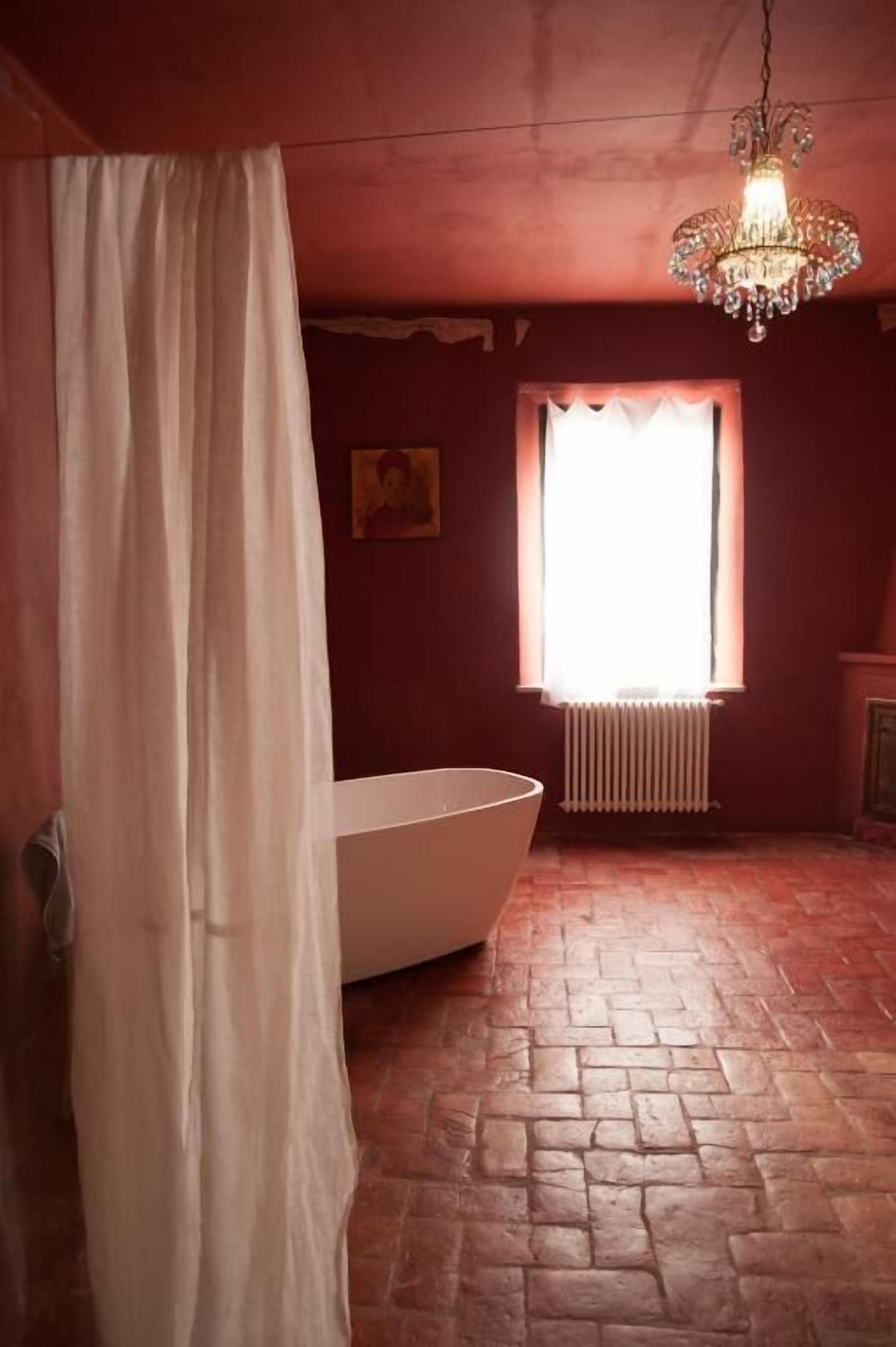 Casa de banho com banheira, radiador e janela com cortinas.