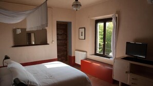 A bedroom with a bed, a television, a window with curtains, a radiator, and a mirror on the wall. - Corte Mantovanella (Porto Mantovano)