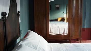 A bedroom with a large bed, wooden wardrobe, and a door leading to another room.