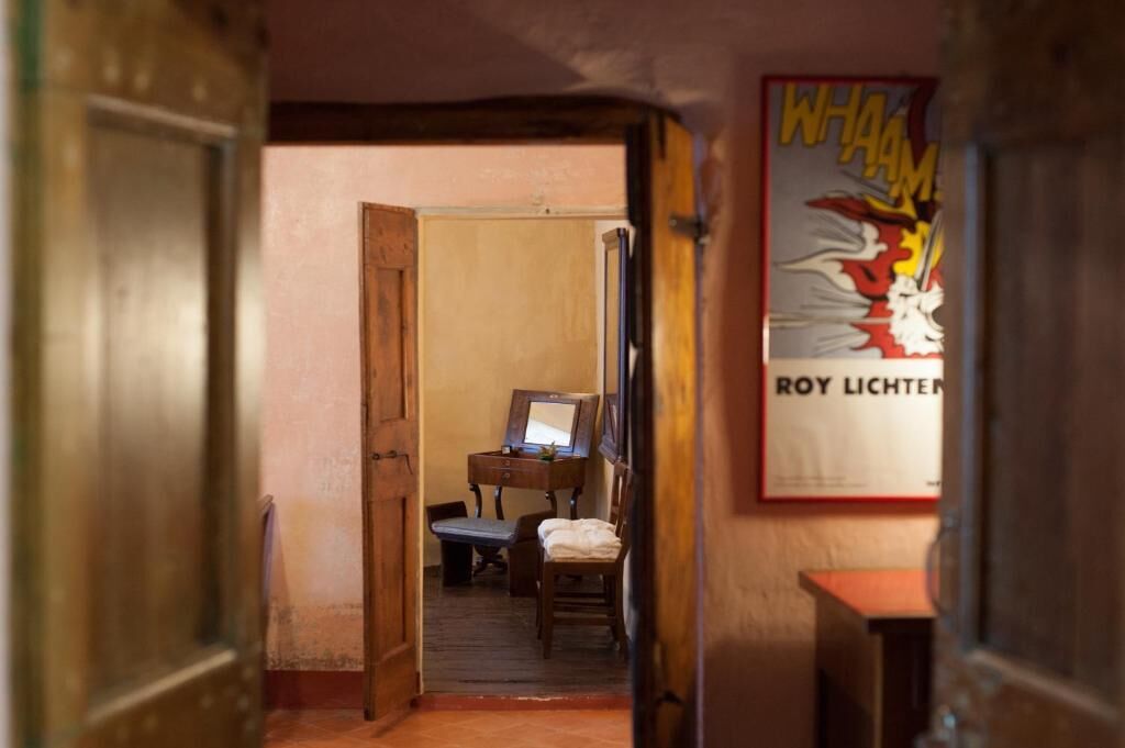 Un pasillo estrecho con un marco de puerta de madera, un escritorio pequeño con una silla, y un cartel en la pared.