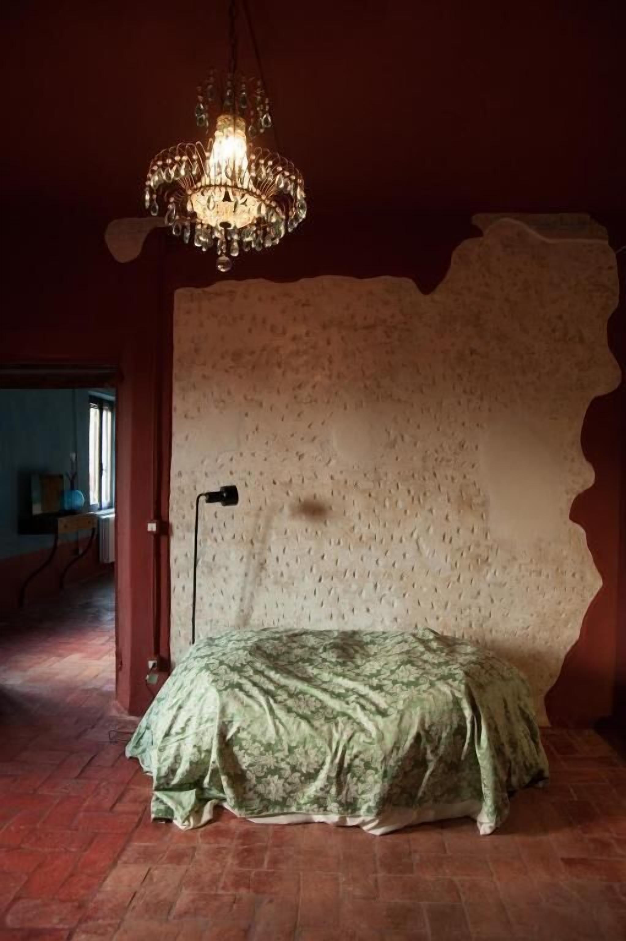 Ein Zimmer mit einem Bett, einer Kristalllüster und einer Wand mit Struktur.