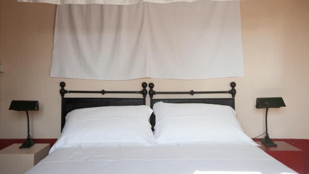 A bed with a black metal frame, white bedding, and two bedside tables with lamps. - Corte Mantovanella (Porto Mantovano)