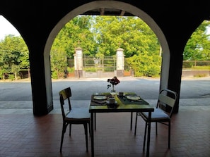 Un área de comedor al aire libre con una mesa para dos, un florero con flores y vista a una entrada porticada.