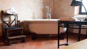 A bathroom with a bathtub, a wooden chair, a small table with a lamp, and a radiator. - Corte Mantovanella (Porto Mantovano)