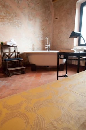 A bathroom with a bathtub, a wooden chair, a small table with a lamp, and a radiator. - Corte Mantovanella (Porto Mantovano)