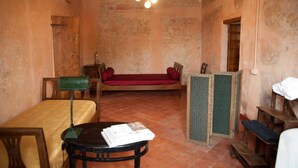 A rustic room with a bed, a desk, a chair, a bench, and a small table with books. - Corte Mantovanella (Porto Mantovano)
