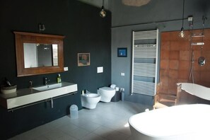 A modern bathroom with a large mirror, a white sink, two toilets, a bidet, and a bathtub. - Corte Mantovanella (Sant'Antonio)
