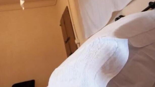 A white bed with a headboard, a white wall, and a door in the background. - Corte Mantovanella (Porto Mantovano)