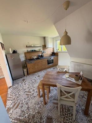 A kitchen with a wooden table and chairs, a refrigerator, and a window.