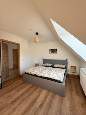 Een slaapkamer met een schuine kap, een bed met bloemenbeddelsels, een hanglamp en een klein nachtkastje.