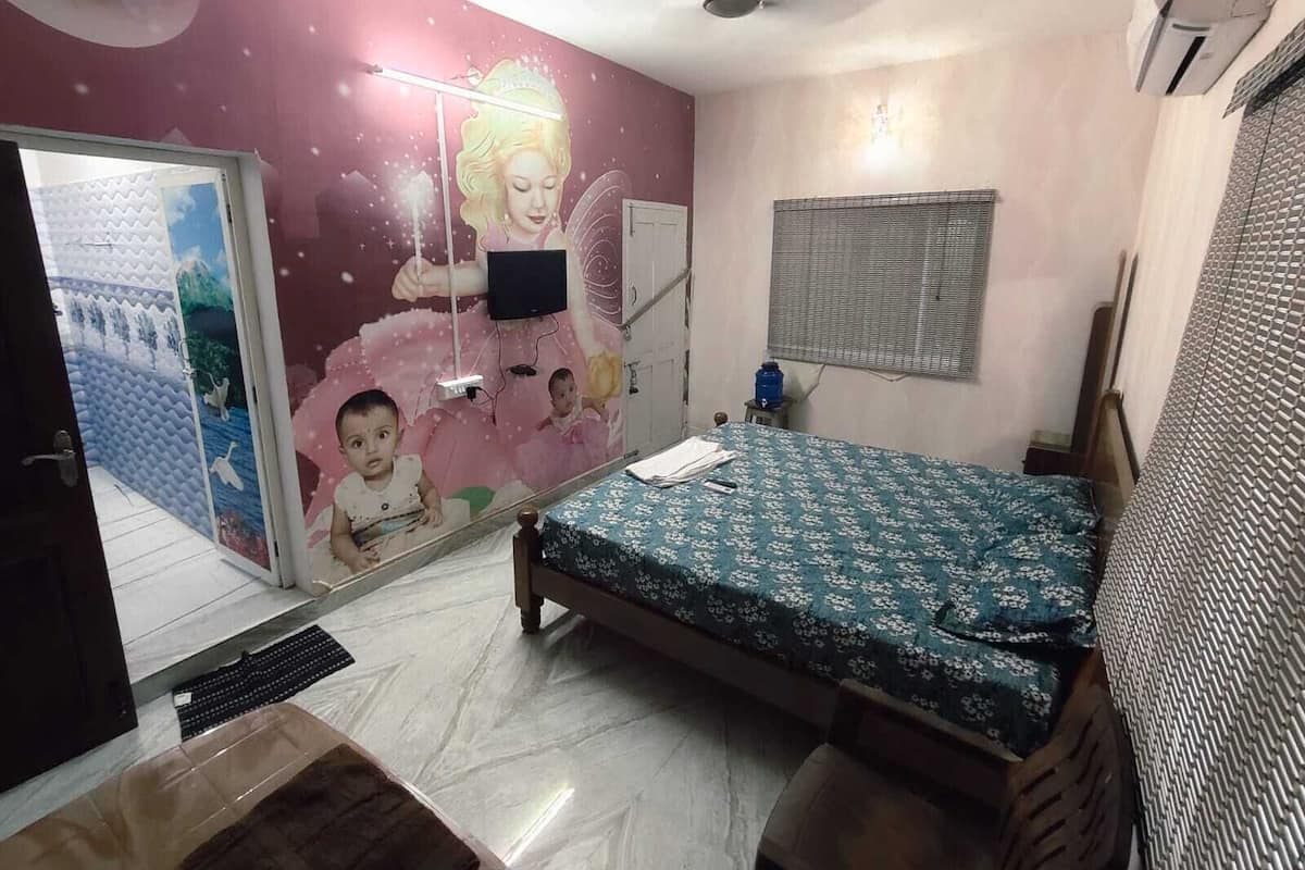 A bedroom with a bed, a wall-mounted TV, a ceiling fan, a window with blinds, and a door with a mirror.