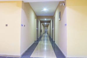 Un pasillo largo y estrecho con piso reflectante, paredes pintadas de amarillo claro y techo con iluminación empotrada.