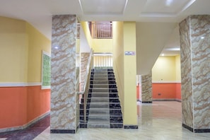 Un vestíbulo de hotel con una escalera de mármol, un cartel de 'NO FUMAR' y vistas al piso superior.