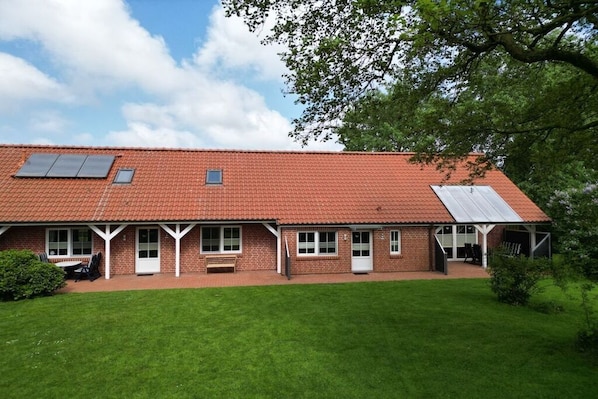 A two-story brick building with a red-tiled roof, a covered patio area, and a well-maintained lawn. - 2 in the Kolbe country house (Norden)