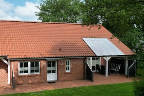 A brick building with a red-tiled roof, a covered patio area, and a garage. - 2 in the Kolbe country house (Norden)