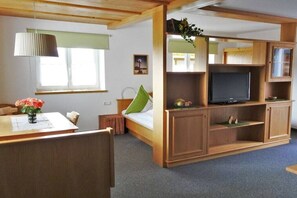 Ein Zimmer mit einem Bett, einem Fernseher, einem Holzschrank, einem Schreibtisch mit Blumenvase und einem Fenster mit Jalousien.