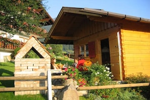Eine Holzhütte mit Steineingang, einer kleinen Veranda und einem Blumengarten.