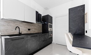 Una cocina moderna con encimeras de mármol negro, horno empotrado y una silla blanca.