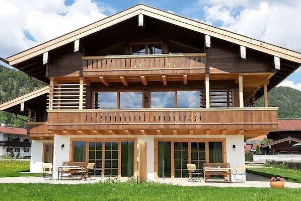 A two-story wooden chalet with a balcony, large windows, and outdoor seating. - "Kaiserwinkl" in the Chalet KAISER (Reit im Winkl)