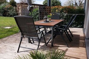 Eine Holzterrasse mit Tisch und Stühlen, umgeben von Pflanzen und einem Zaun.