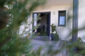 Ein moderner Gebäudeeingang mit Glastür, einem kleinen Blumentopf und einem Metallgeländer.