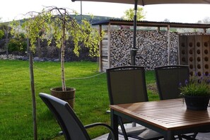 Eine Terrasse mit Tisch und Stühlen, einem Blumentopf und einem Holzzaun im Hintergrund.