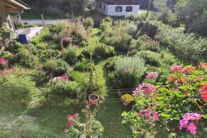 Un jardin avec différentes plantes et fleurs, une clôture en bois et un bâtiment blanc en arrière-plan.
