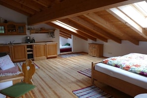 Ein gemütliches Schlafzimmer im Dachgeschoss mit Holzbalken, einem Etagenbett, einem Schreibtisch und einer Küchenzeile.